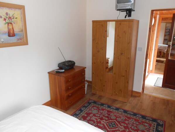 A bedroom with a wooden dresser, a TV on a stand, a bed, and a mirror in the wardrobe. - Birchdale Apartment (Rathdrum)