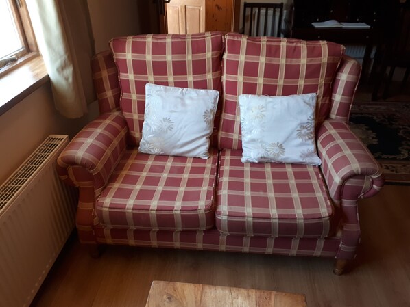 A red and white checkered sofa with floral cushions in a room with wooden flooring and a radiator. - Birchdale Apartment (Rathdrum)
