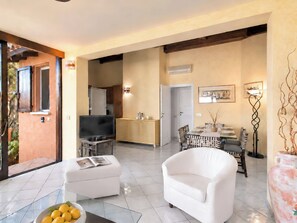 A modern living room with a flat-screen TV, a white sofa, and a dining area with a table set for four. - Beautiful apartment for 4 people with A/C, WIFI, TV and patio (Olbia)