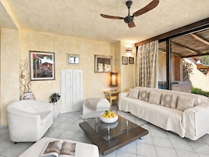 A modern living room with a ceiling fan, a sofa, a coffee table with a bowl of fruit, and a bookshelf.