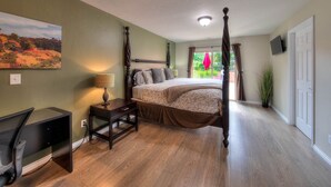 A bedroom with a four-poster bed, a desk with a computer, a painting on the wall, and a view of greenery outside. - Stunning Moab townhome on the golf course! (Moab)