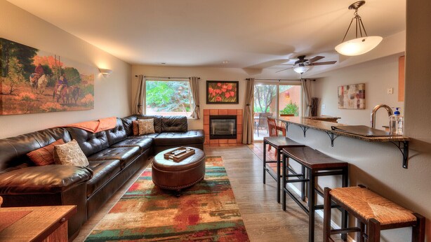 A living room with a leather sofa, a fireplace, a dining area with a wooden table, and a view of the outdoors. - Stunning Moab townhome on the golf course! (Moab)