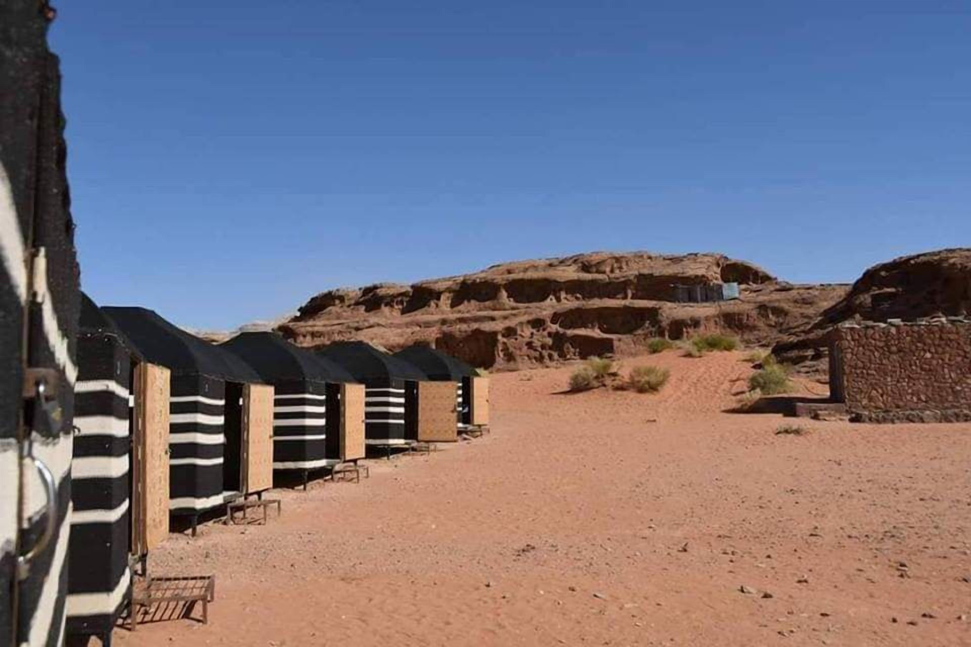 En række strandhytter med striber i et ørkenlandskab med en stor klippeformation i baggrunden.