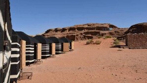 A row of striped beach huts in a desert setting with a large rock formation in the background. - Ultimate (Wadi Rum)
