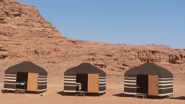 Three small, striped, tent-like structures in a desert setting with rocky hills in the background. - Ultimate (Wadi Rum)