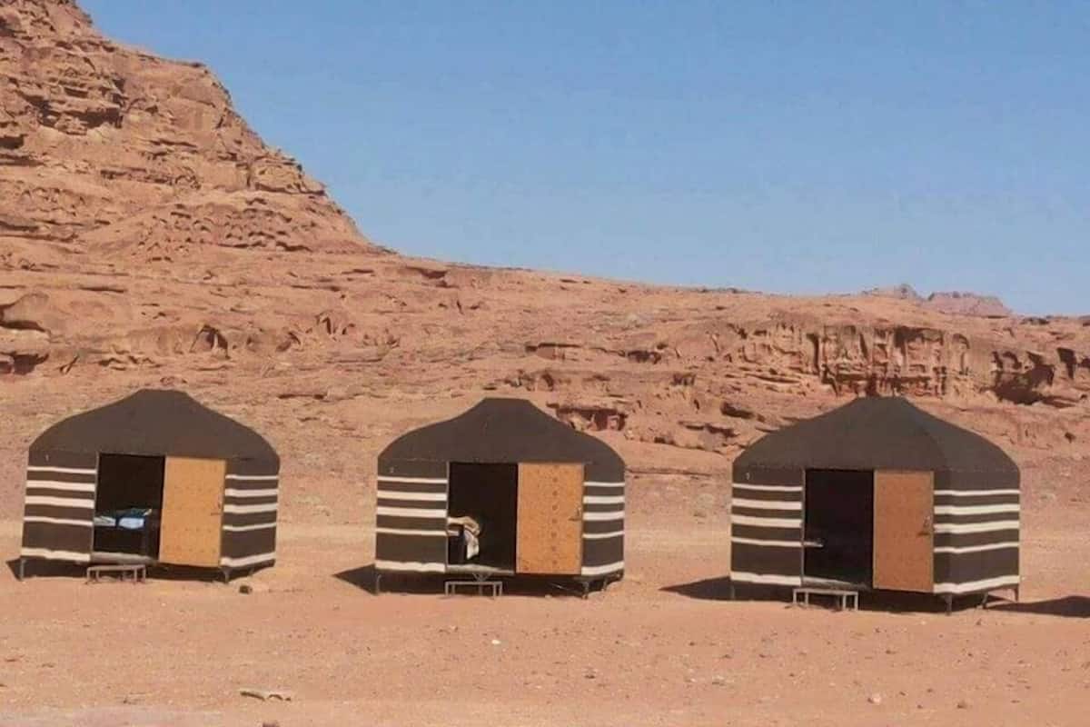 Three small, striped, tent-like structures in a desert setting with rocky hills in the background.