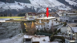 A residential area with houses, a prominent red arrow pointing to a specific building, and a snowy mountainous backdrop. - Apartment #1 in Haus Sophia with a unique view (DG) (Oberperfuss)