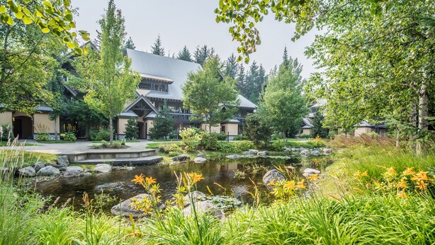 A traditional Japanese-style building with a koi pond surrounded by lush greenery and flowering plants.