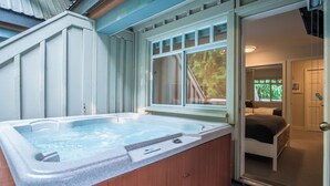 A hot tub in a room with a bed and a window overlooking greenery.