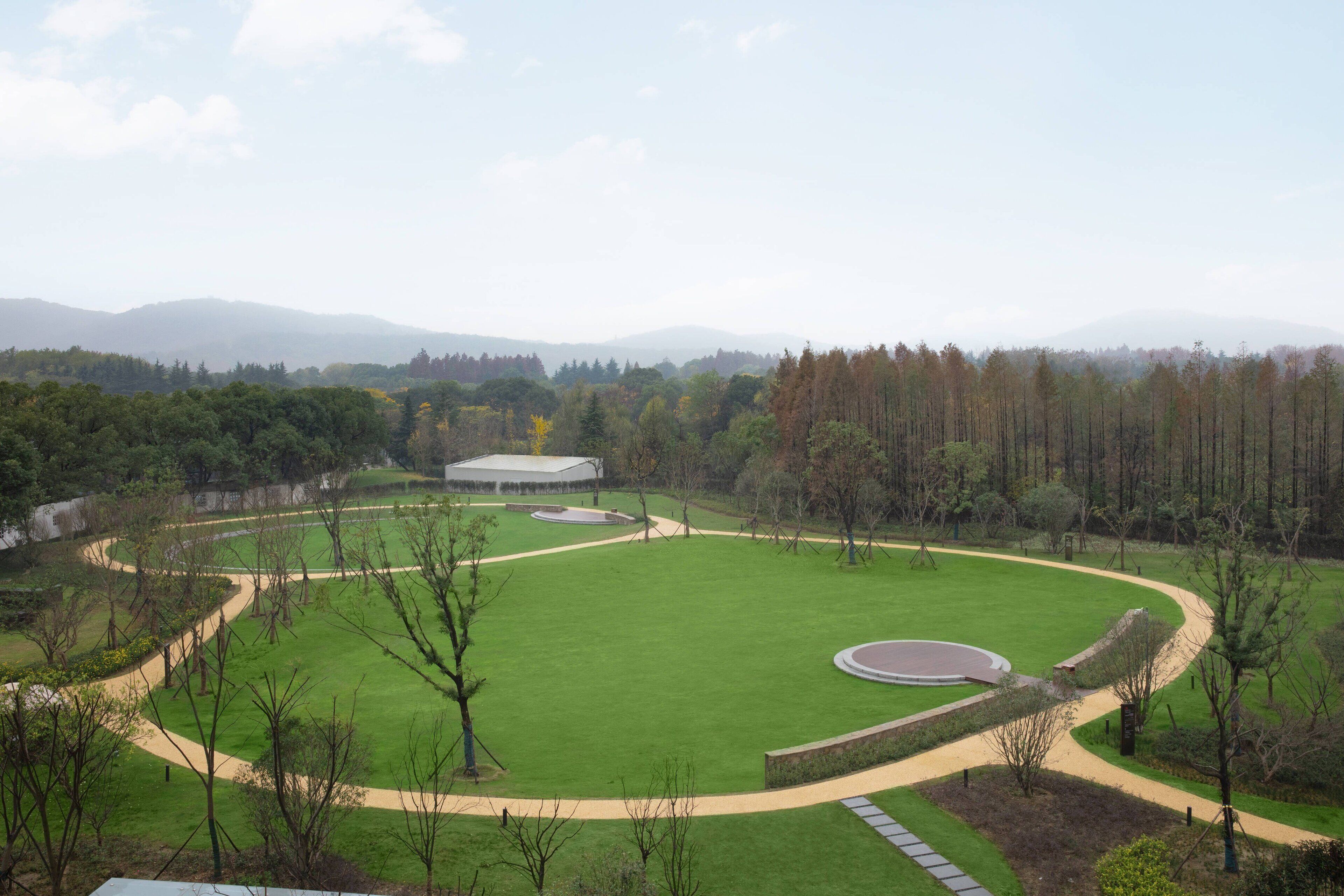 Una amplia zona verde con un camino circular y un edificio al fondo.