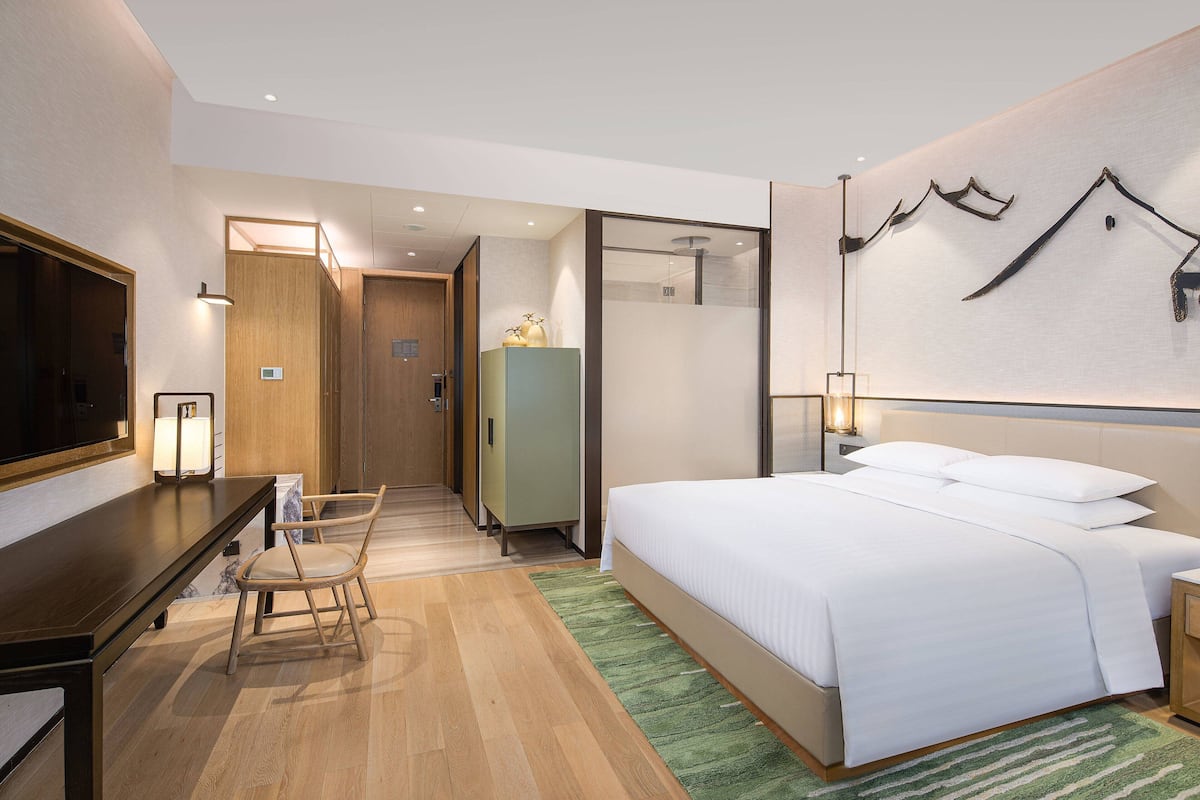 Habitación de hotel con cama, escritorio, silla, televisor y una obra de arte colgada en la pared.