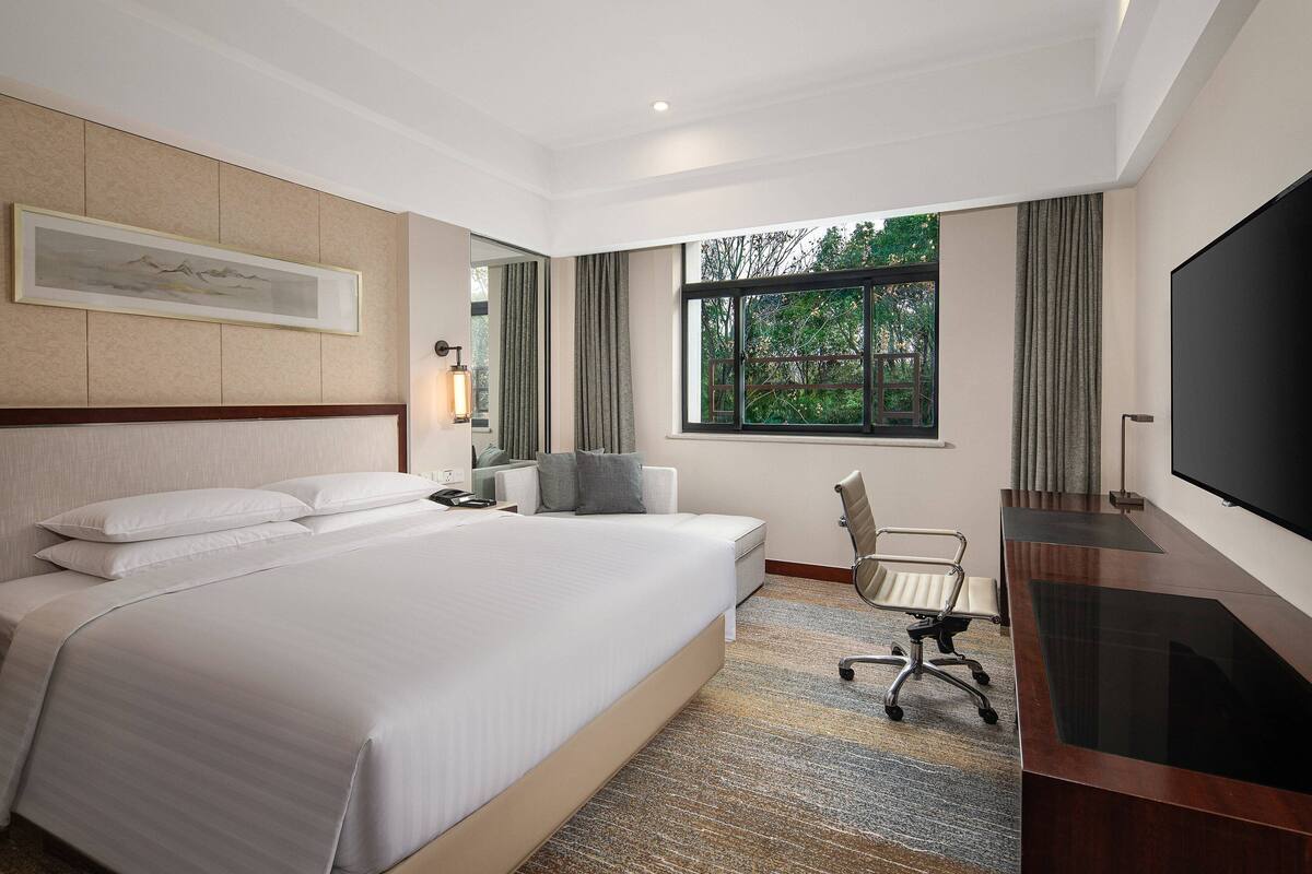 Habitación de hotel con una cama grande, un escritorio con televisor de pantalla plana, una silla y una ventana con cortinas.