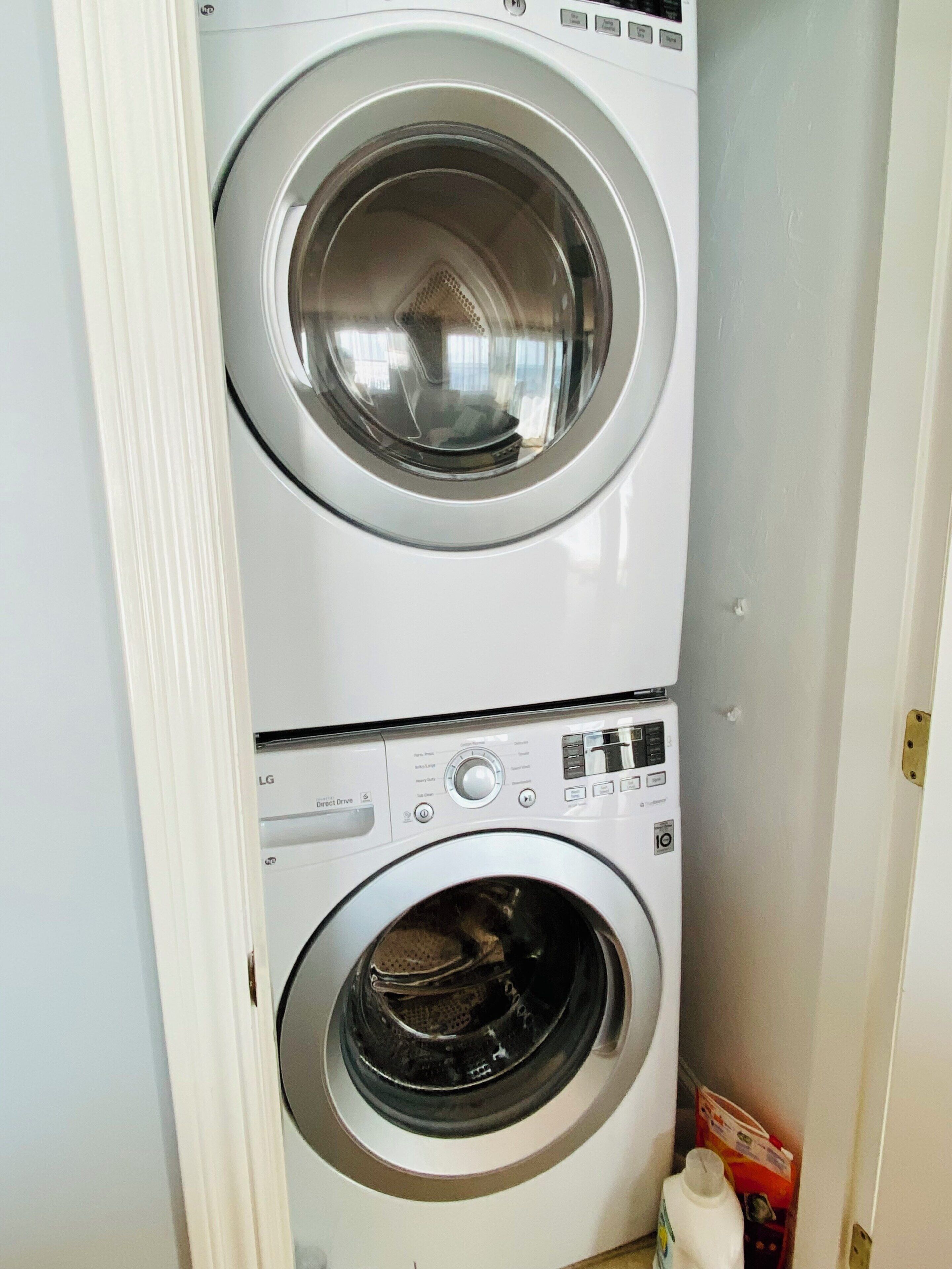 A stacked washer and dryer unit with a control panel and a small storage area with a bag and bottle.