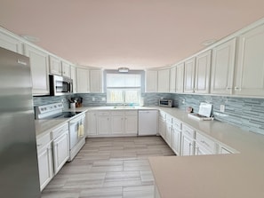 A modern kitchen with white cabinets, a stainless steel refrigerator, a microwave, and a dishwasher.