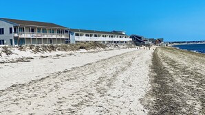 Un hôtel situé en bord de mer, doté de nombreux balcons, avec une plage de sable fin juste devant et un ciel bleu azur.