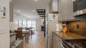 Una cocina moderna con electrodomésticos de acero inoxidable, un comedor con mesa de vidrio y una escalera que conduce a un nivel superior.