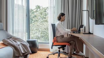 A hotel room with a bed, a desk with a laptop, a coffee cup, and a window with curtains.