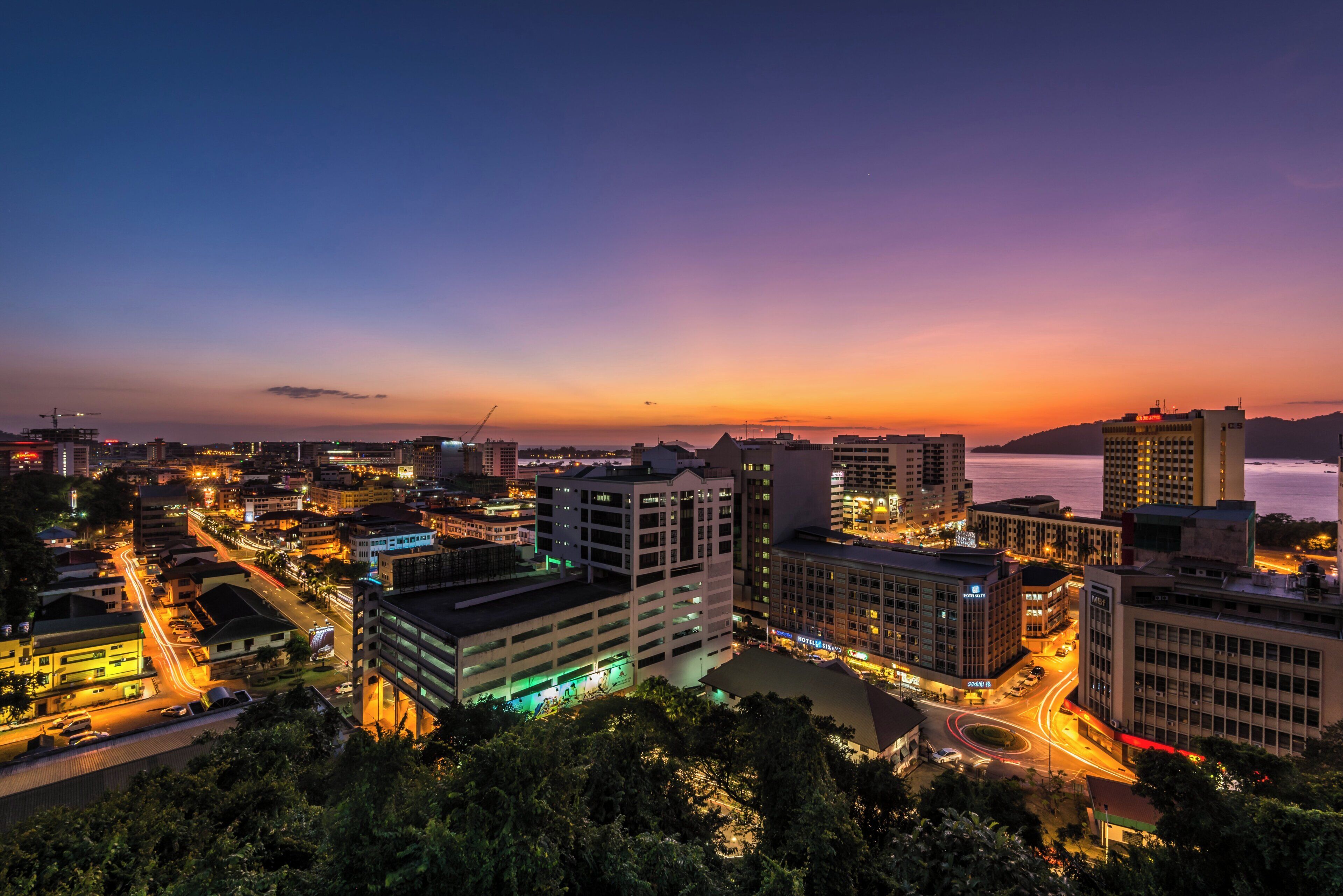 A cityscape at dusk with illuminated buildings and a view of the water.