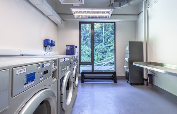 A laundry facility with multiple washing machines, a dryer, and a view of greenery through a large window. - Holiday Inn Express Kota Kinabalu City Centre by IHG (Kota Kinabalu)