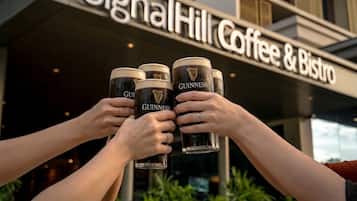 Un edificio con un letrero que dice 'Signal Hill Coffee & Bistro' y tres personas sosteniendo vasos de Guinness.