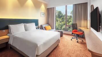 A hotel room with a large bed, a desk with a chair, a television, and a window with curtains.