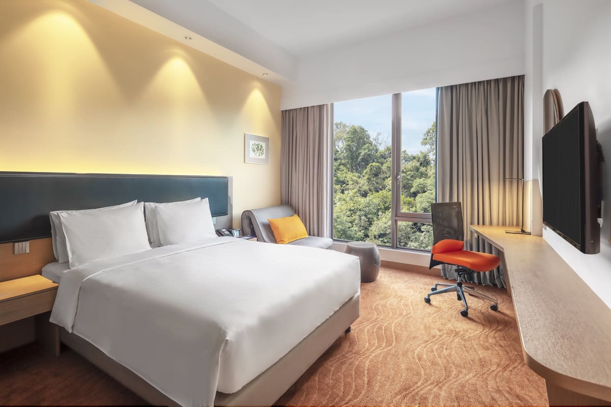 Ein Hotelzimmer mit einem großen Bett, einem Schreibtisch mit Stuhl, einem Fernseher und einem Fenster mit Vorhängen.