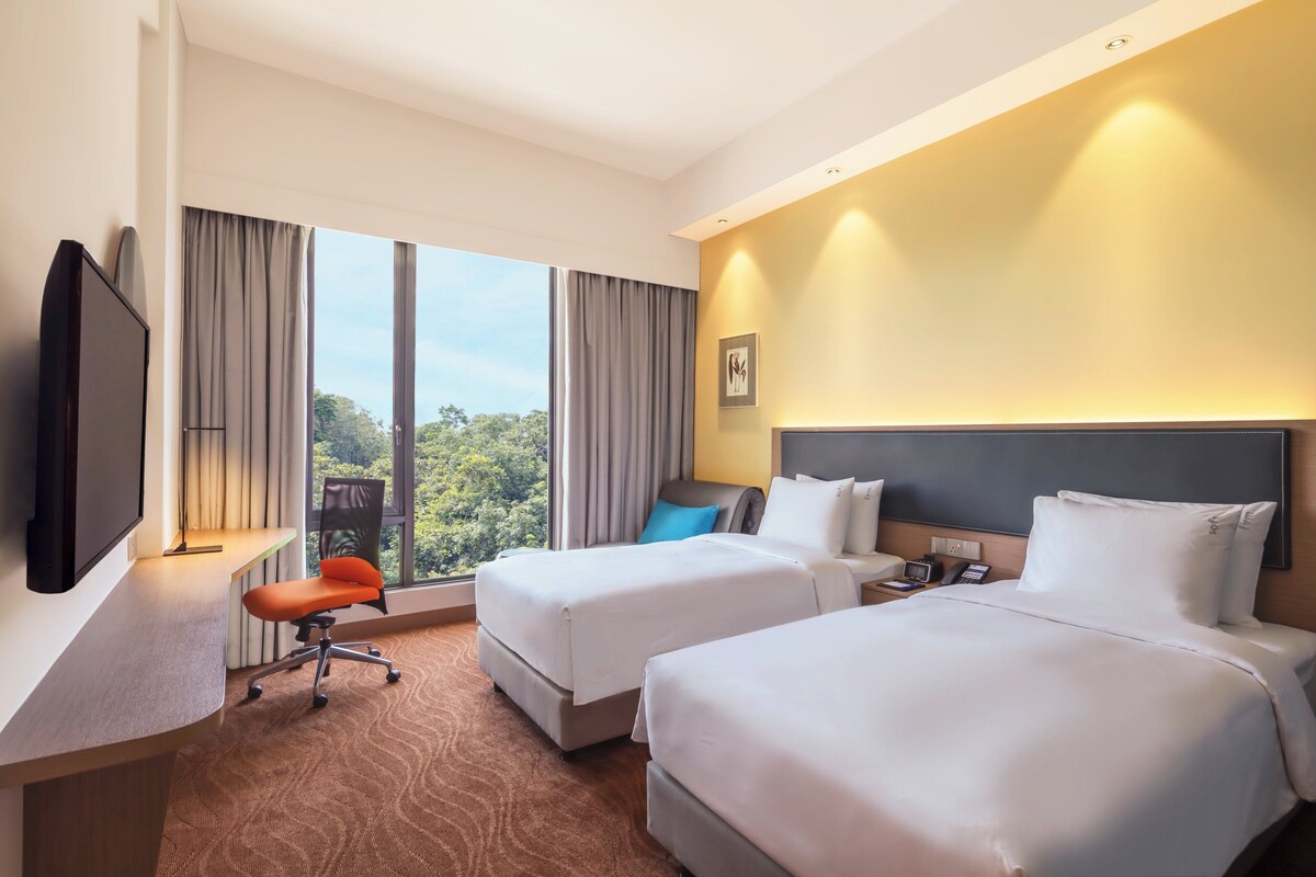 A hotel room with two beds, a desk with a TV, a chair, and a view of the outdoors.
