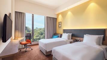 A hotel room with two beds, a desk with a TV, a chair, and a view of the outdoors.