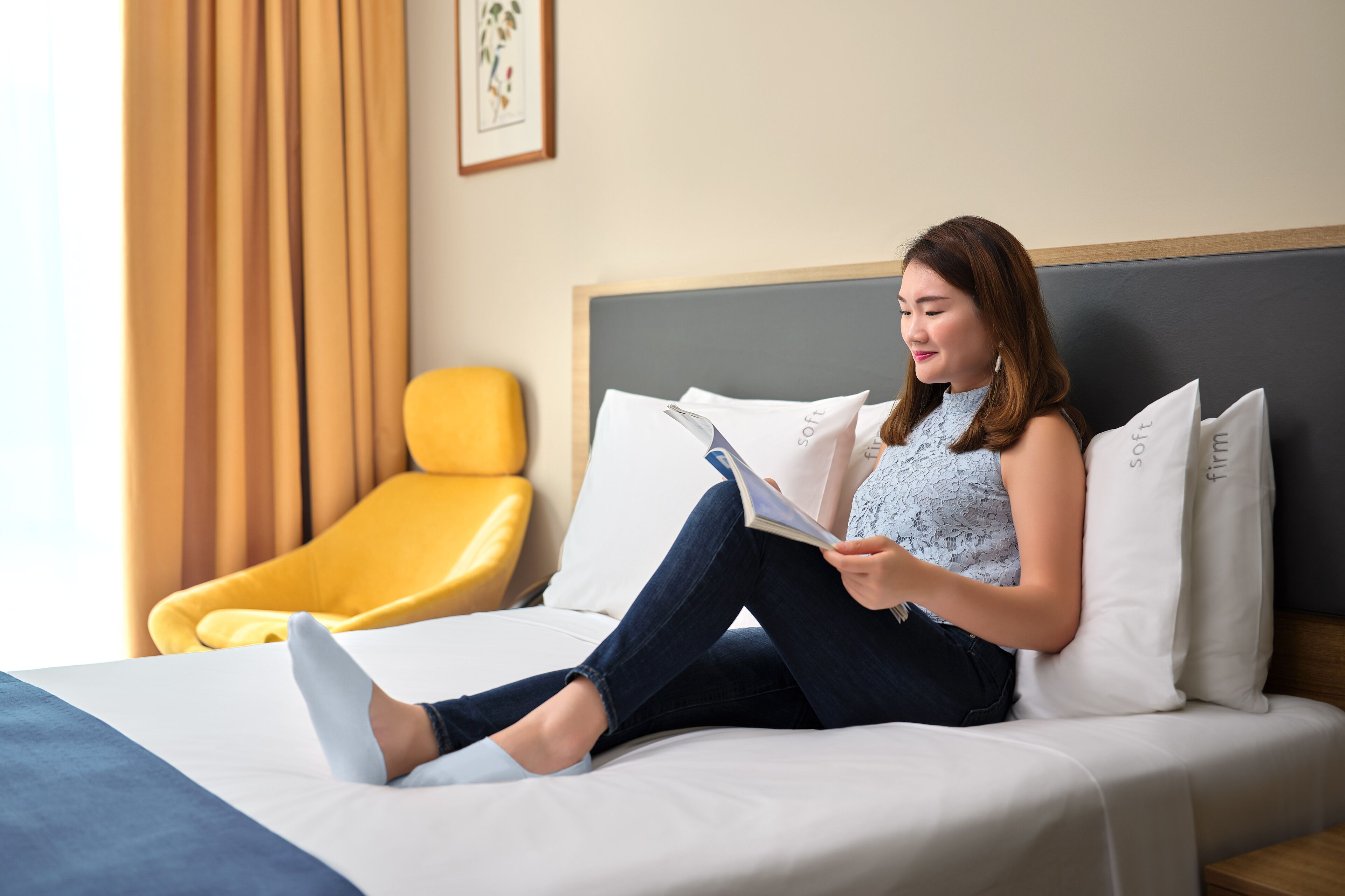 A woman sitting on a bed in a hotel room, reading a book.