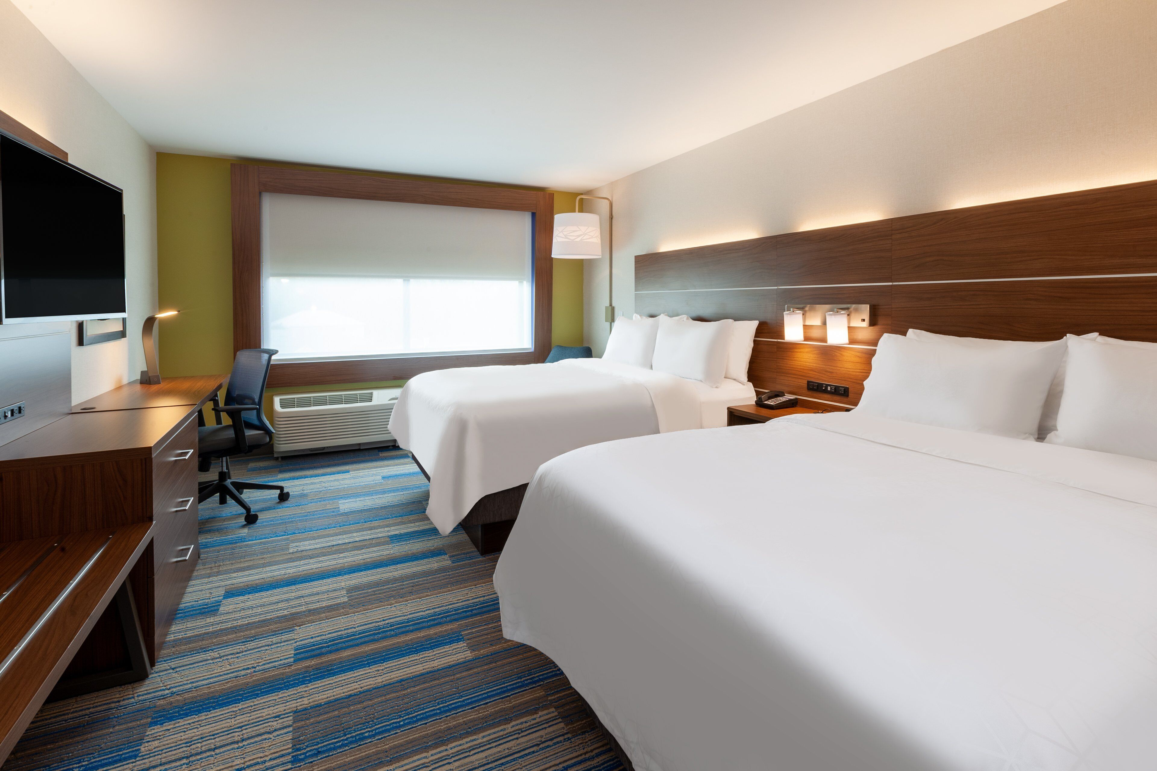 Ein Hotelzimmer mit zwei Betten, einem Schreibtisch, einem Fernseher und einem großen Fenster.