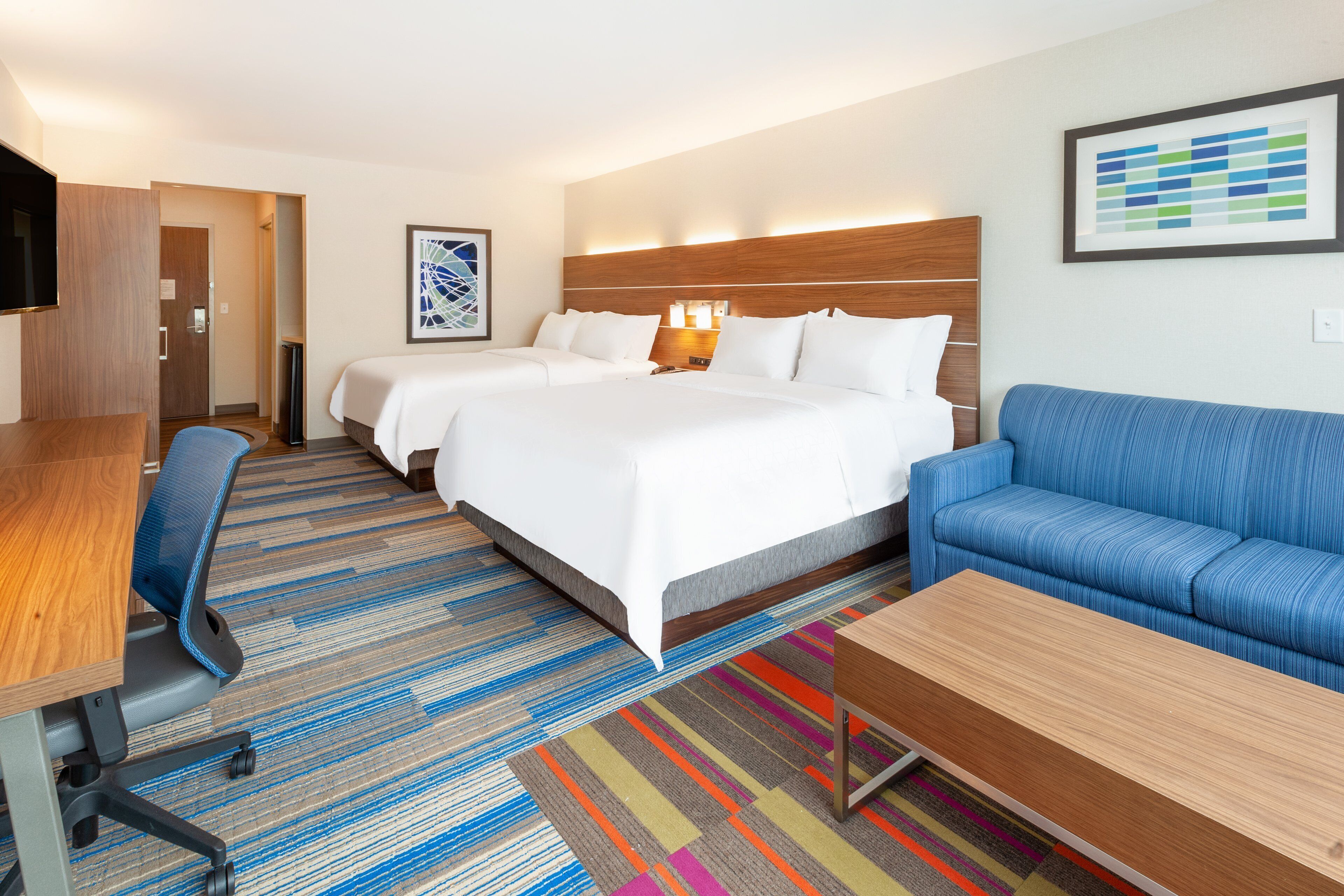 Una habitación de hotel con una cama grande, un sofá azul, un escritorio de madera y una alfombra colorida a rayas.