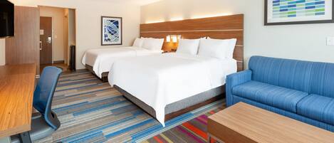 Una habitación de hotel con una cama grande, un sofá azul, un escritorio de madera y una alfombra colorida a rayas.