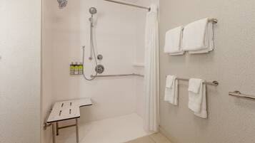 Casa de banho moderna com chuveiro amplo, lavatório branco e várias toalhas penduradas num porta-toalhas.