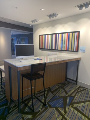 A modern office space with a glass desk, a black chair, and a colorful striped artwork on the wall.