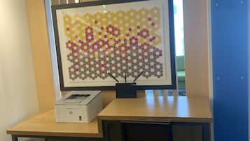 A workspace with a desk, chair, printer, and a framed artwork.