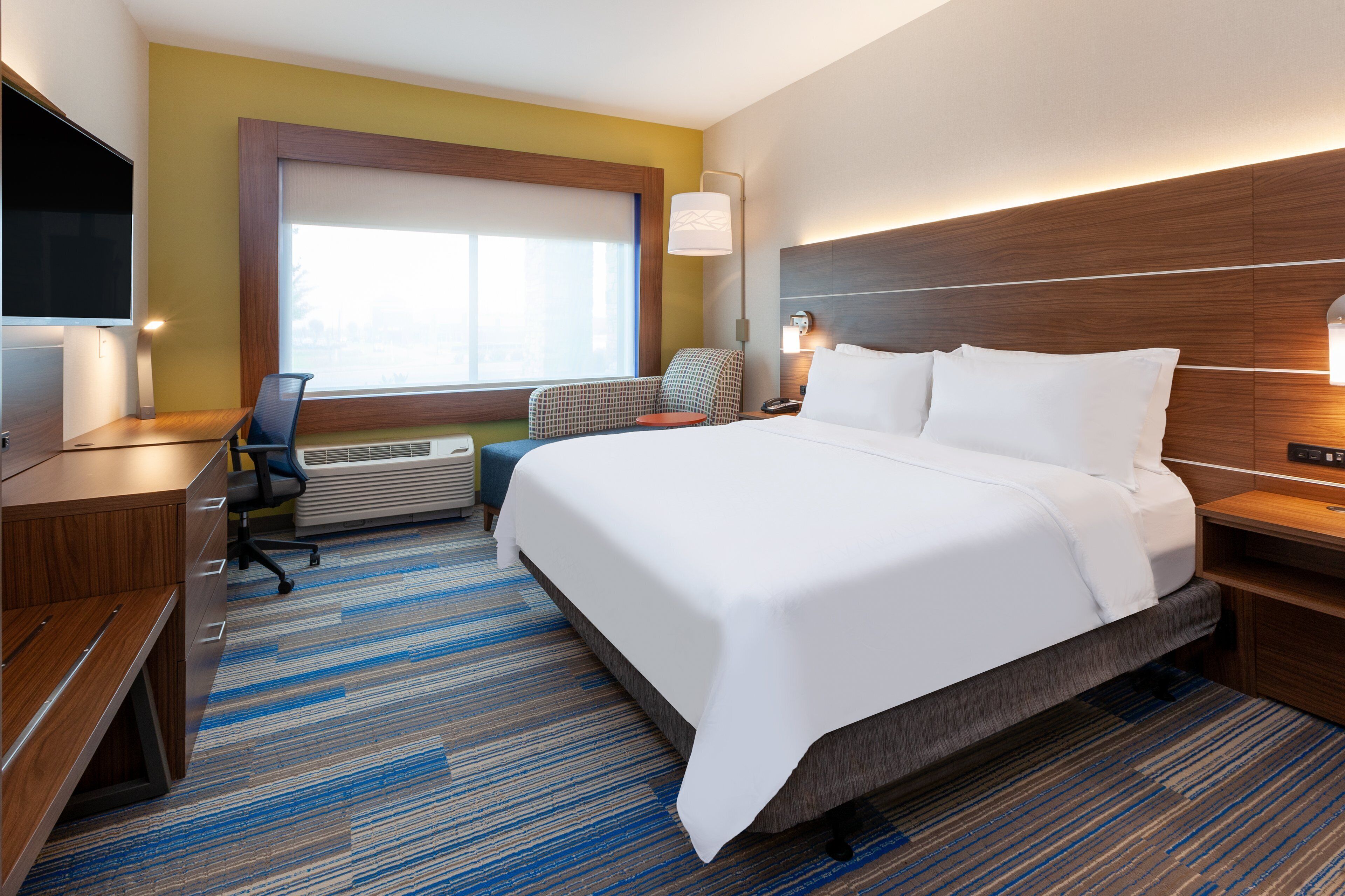 A hotel room with a large bed, a desk, a chair, a TV, and a window.