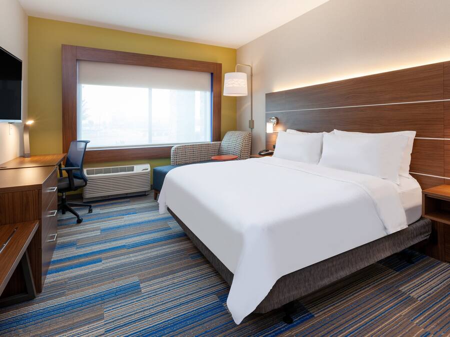 A hotel room with a large bed, a desk, a chair, a TV, and a window.