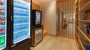 A vending machine area with Coca-Cola and Dasani water bottles, a small refrigerator, and a snack shelf. - Holiday Inn Express & Suites Brunswick - Harpers Ferry Area by IHG (Knoxville)