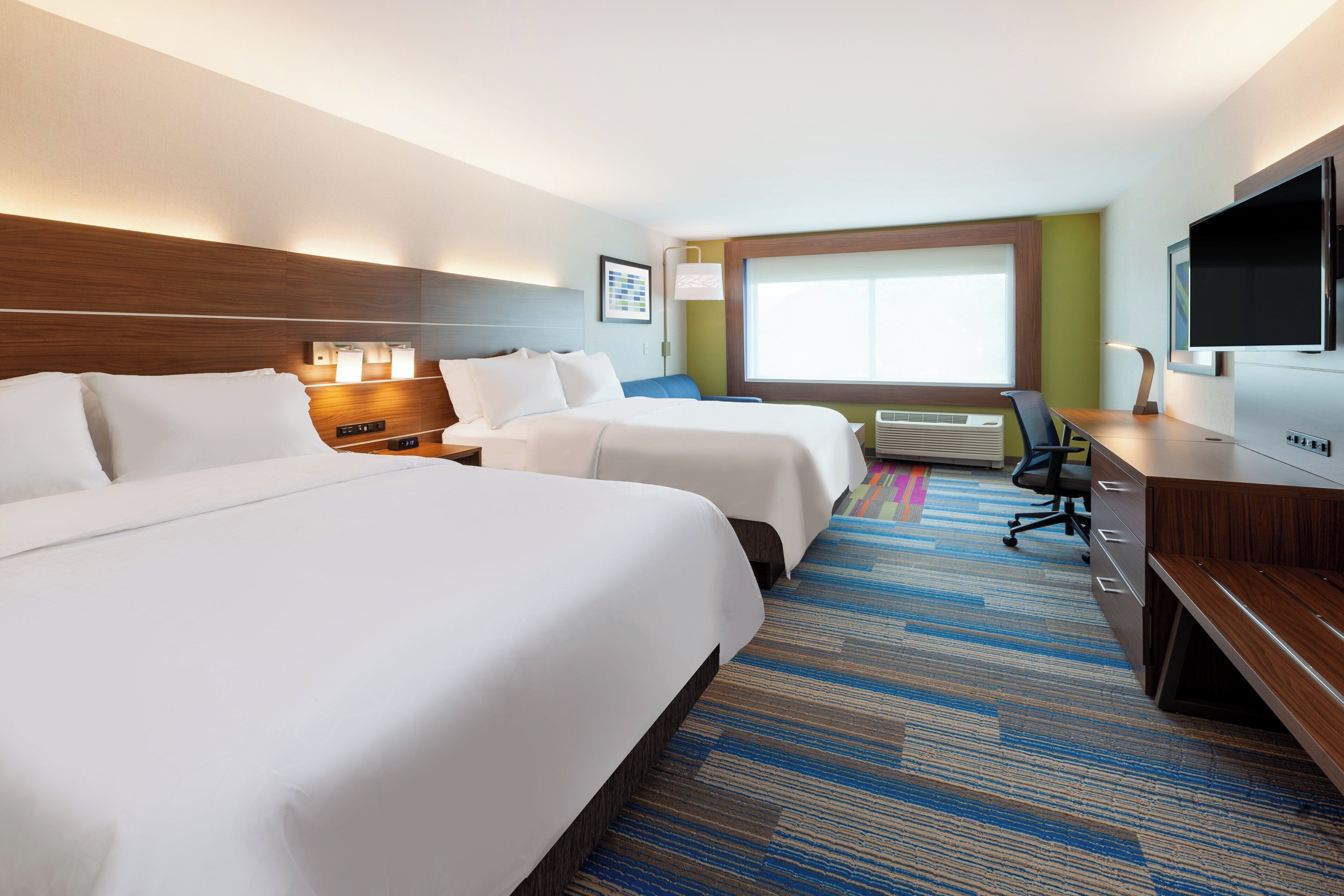 A hotel room with two beds, a desk, a television, and a window with blinds.