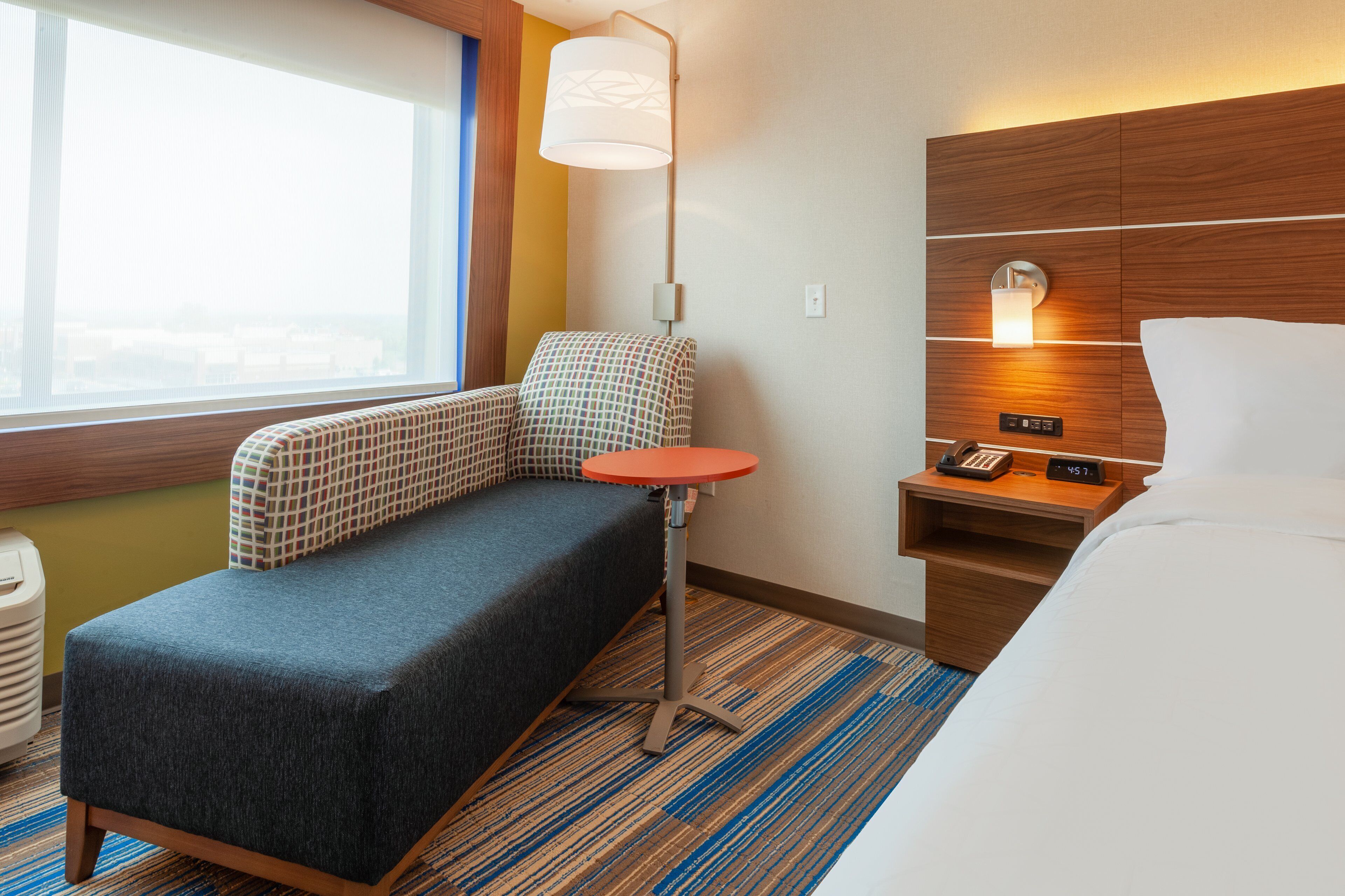 Una habitación de hotel con cama, sofá, una mesita, lámpara y mesita de noche con teléfono y reloj.