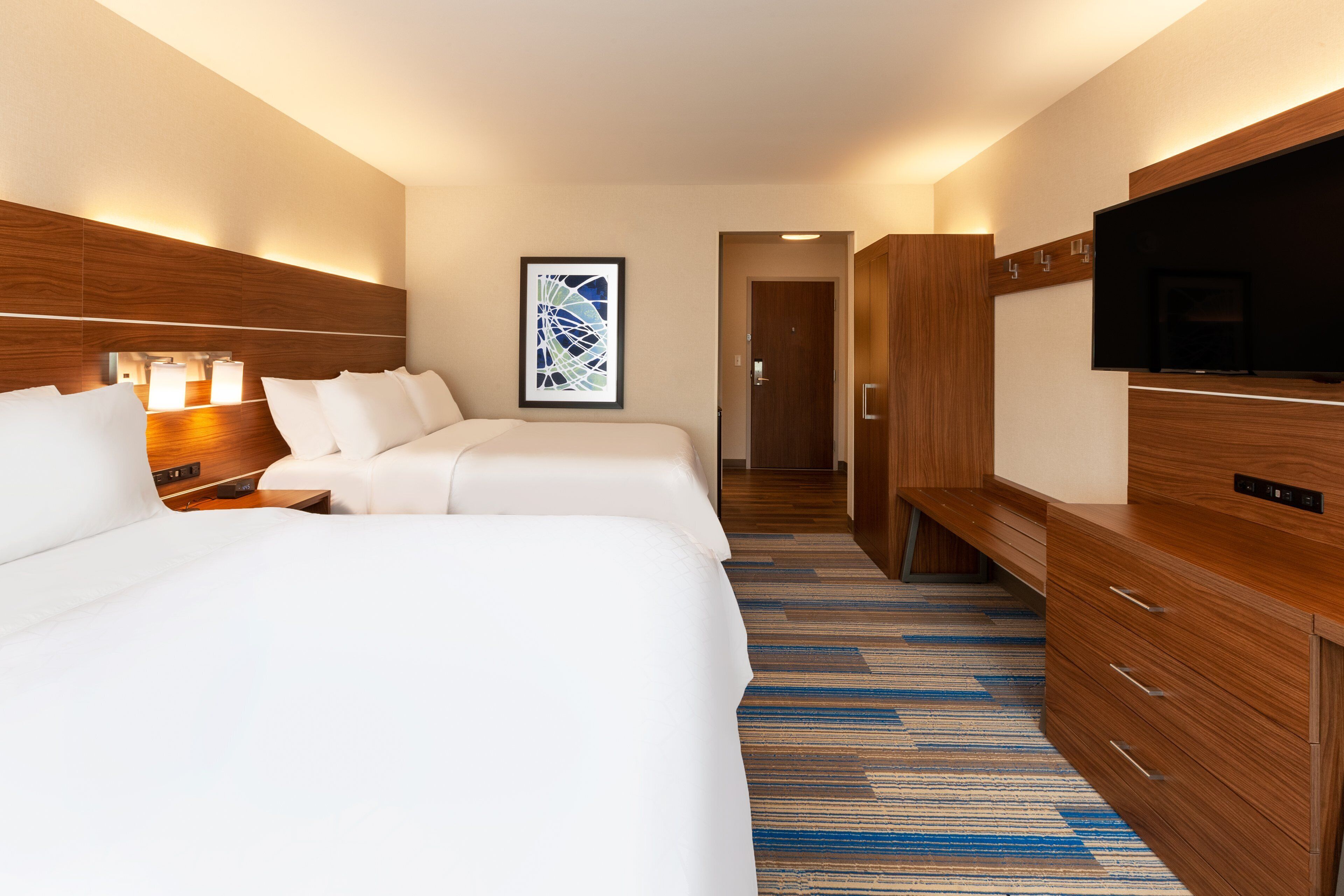 Habitación de hotel con dos camas, un televisor de pantalla plana, un aparador de madera y una obra de arte abstracta enmarcada en la pared.