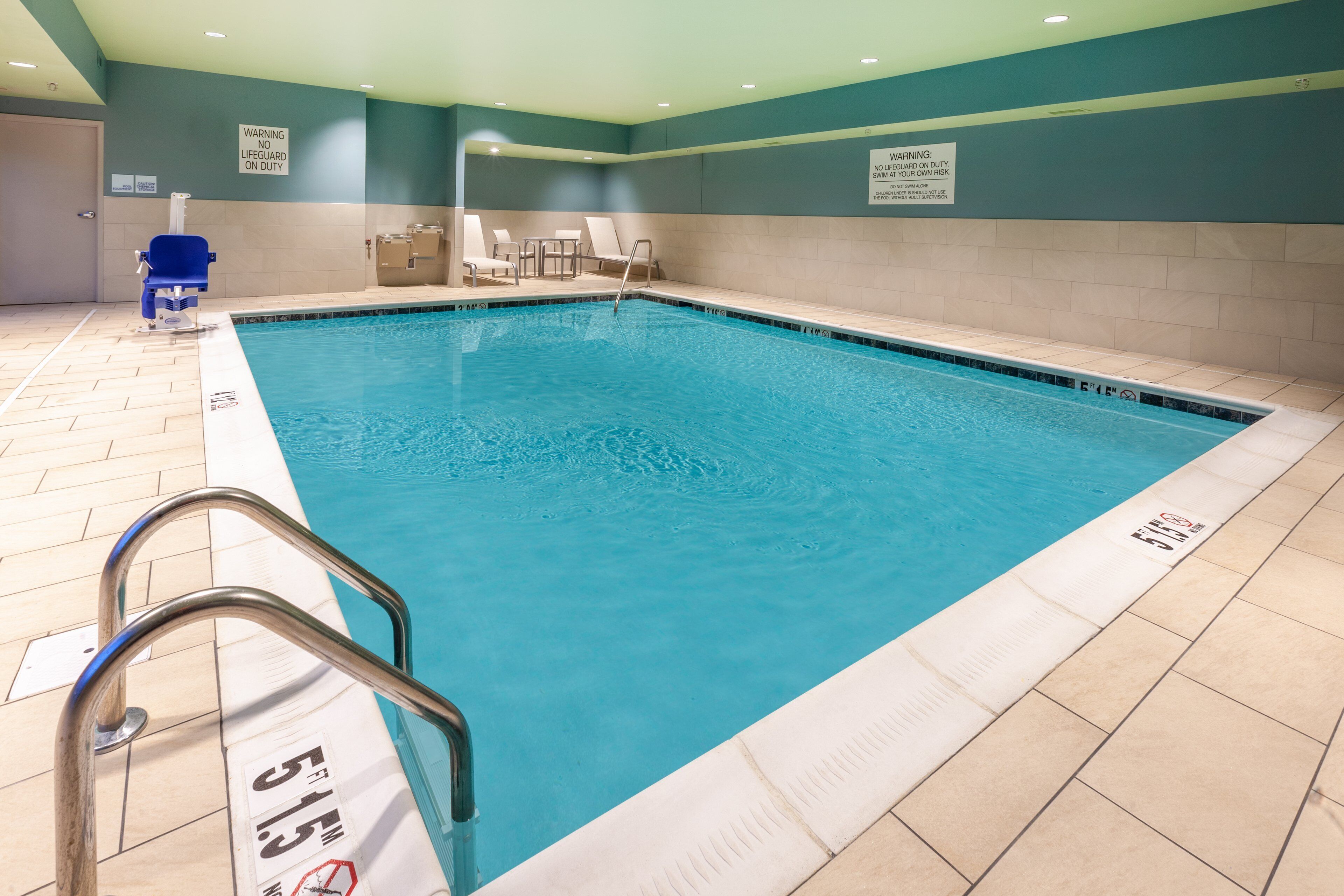 Una piscina interior con un elemento acuático azul, una silla de salvavidas y un letrero de advertencia en la pared.