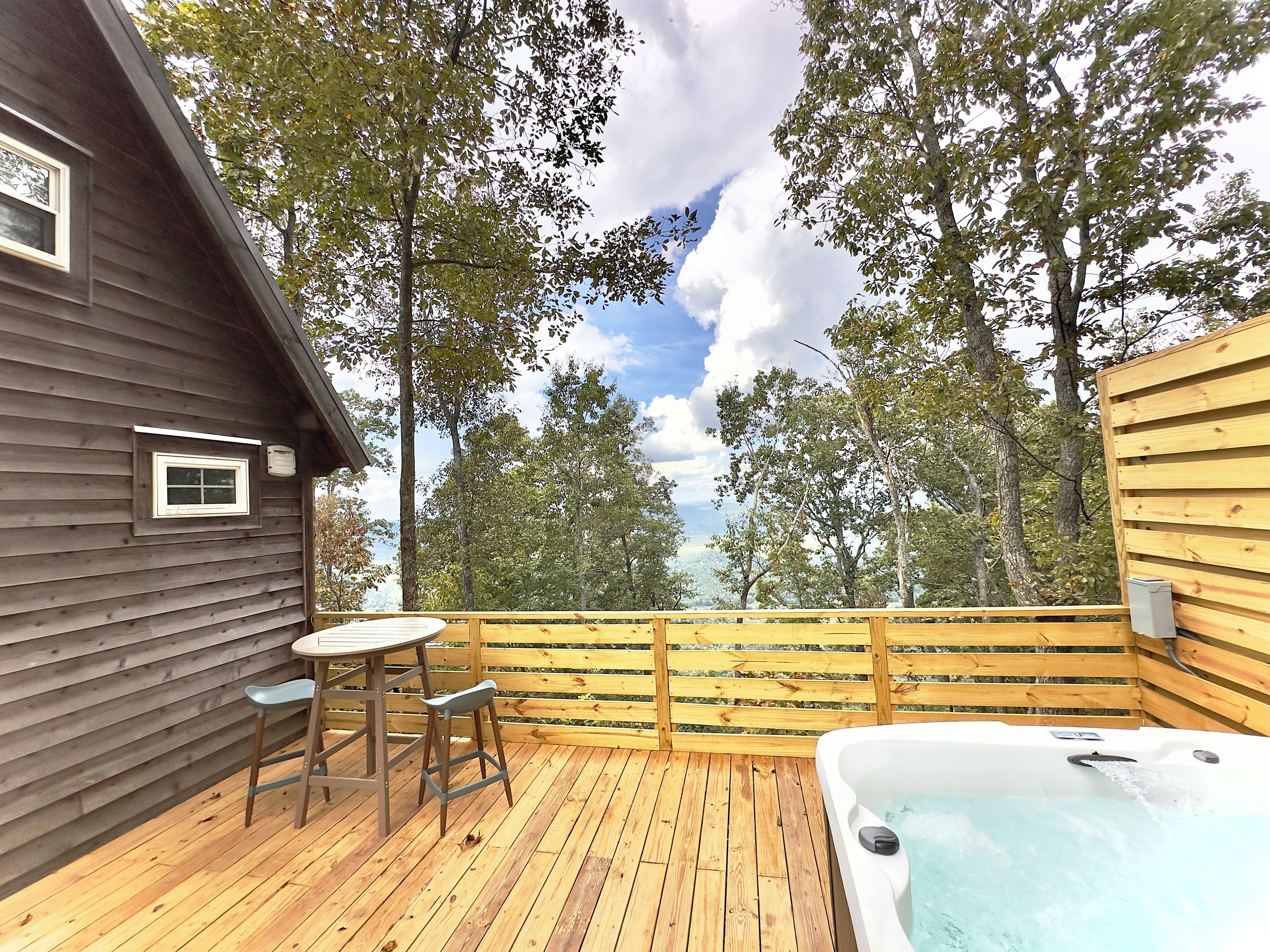 A wooden deck with a hot tub, a table, and two chairs.