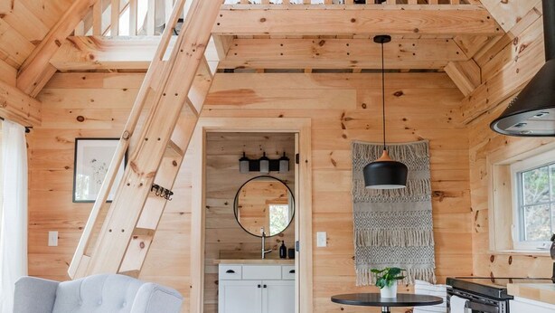Un intérieur de chalet chaleureux avec une chambre à coucher située en mezzanine, un coin repas et une cuisine.