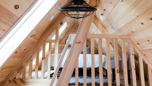 Une chambre mansardée en bois, avec un plafond en pente, un luminaire noir suspendu et un lit recouvert de linge de lit blanc.