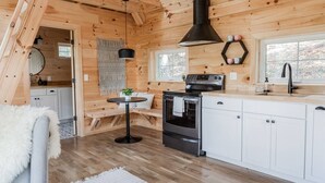 L’intérieur chaleureux d’un chalet, avec un revêtement mural en bois, un coin repas doté d’une table ronde, une cuisine équipée d’une cuisinière et d’un four, et une grande fenêtre.