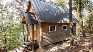 Une cabane en bois avec un toit en pente, une véranda à l’avant et une petite fenêtre.