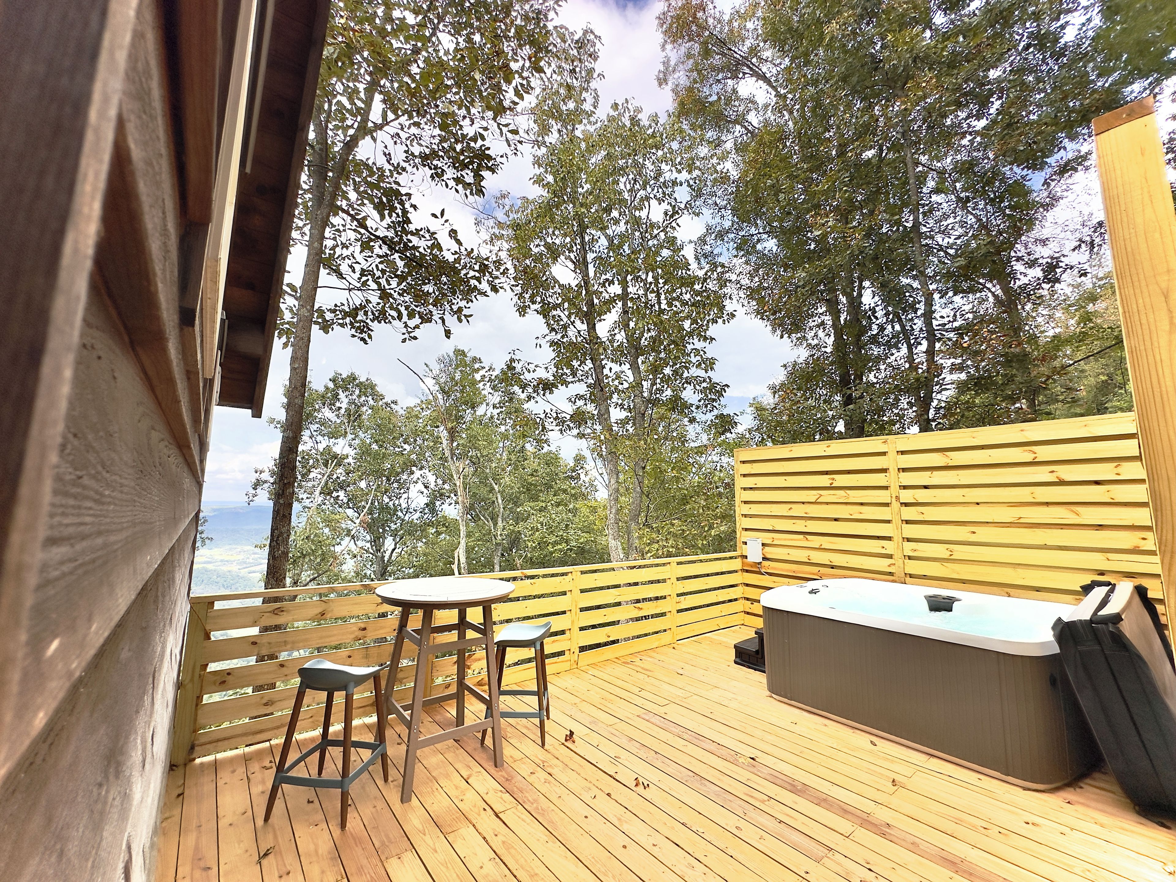 A wooden deck with a hot tub, two bar stools, and a table.