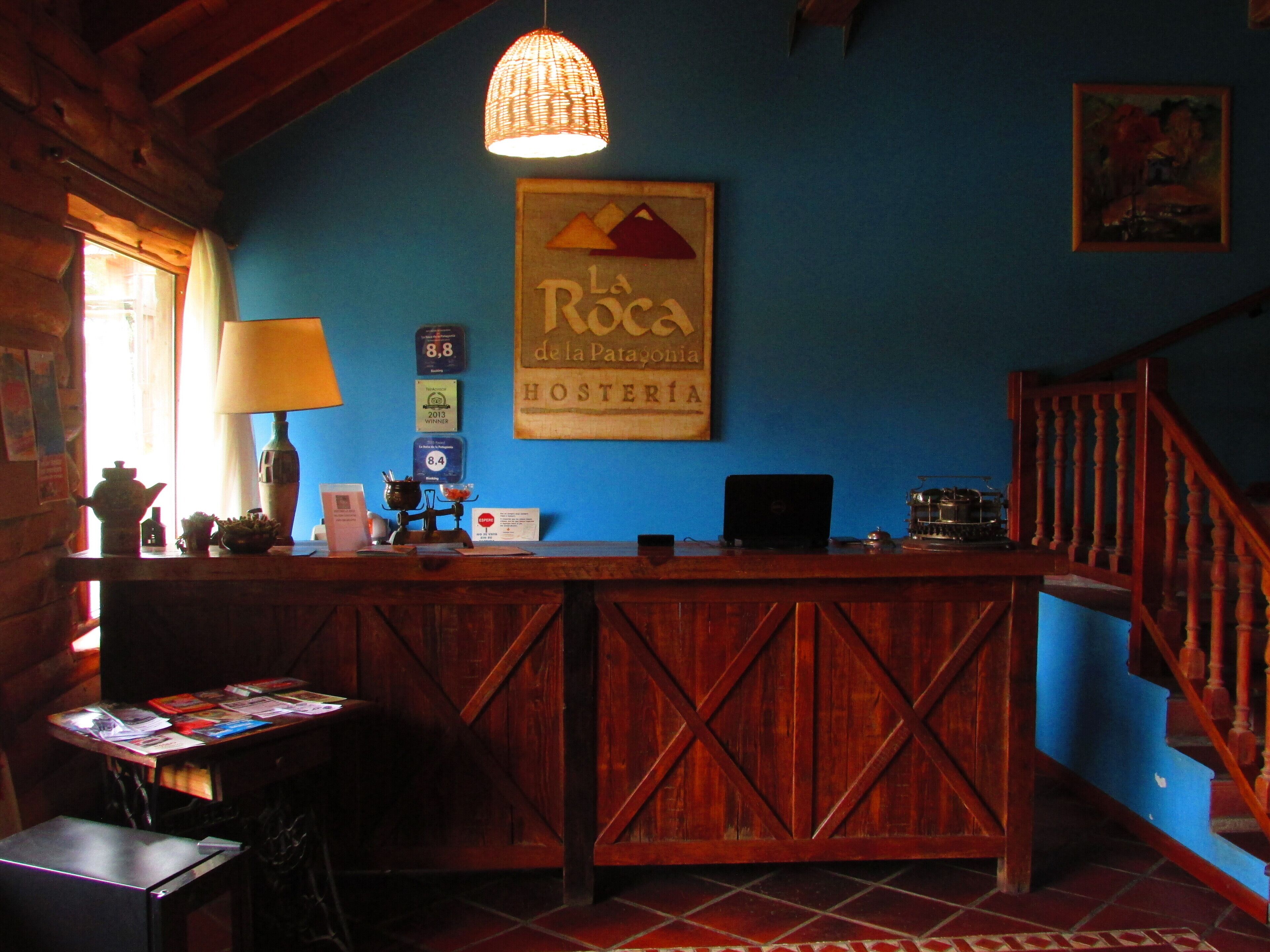 A rustic wooden reception desk with a sign above it, a lamp, and a computer on the desk.