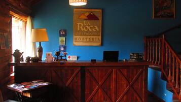 A rustic wooden reception desk with a sign above it, a lamp, and a computer on the desk.